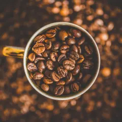 Tazza piena di chicchi di caffè tostati, un invito a gustare la bevanda che fa passare la fame.
