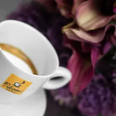Tazza di caffè con logo Filicori. Un macchiatone o un macchiato? La bellezza dei fiori viola fa da sfondo.