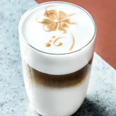 Un delizioso cappuccino freddo con schiuma decorata a forma di fiore, servito in un bicchiere trasparente.