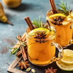 Due bicchieri di grog bevanda calda, guarniti con cannella, anice stellato, limone e rosmarino.