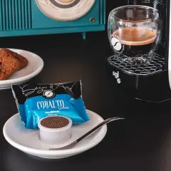 Un caffè decaffeinato pronto per essere gustato, accompagnato da biscotti al cioccolato e una macchina da caffè moderna.