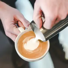 Mani esperte versano latte per cappuccino, creando un disegno sulla schiuma.