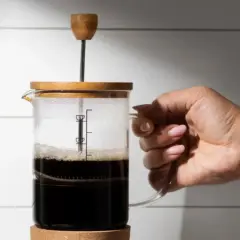 Mano che tiene una french press con caffè scuro. La scelta del quale caffè per french press è fondamentale per un aroma intenso.