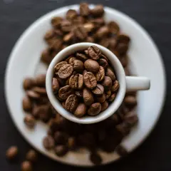 Chicchi di caffè tostati in una tazzina bianca, pronti per la tua **caffeina pre workout**. Un'esplosione di energia naturale.