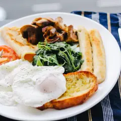 Un piatto ricco per una colazione continentale: uova in camicia, pomodoro, funghi, spinaci, pane tostato e salsicce.