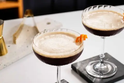 Due cocktail scuri con schiuma chiara, guarniti con scorza d'arancia. Un'idea per un caffè e succo d'arancia rivisitato.