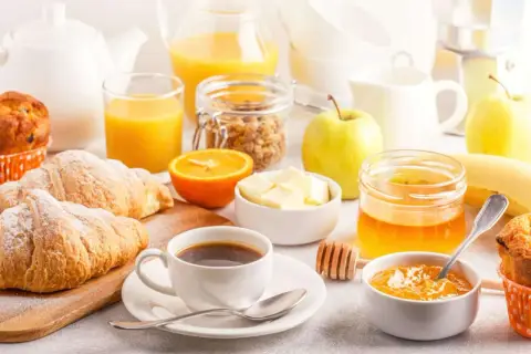 Un tavolo imbandito con croissant, caffè, succo d'arancia, frutta e marmellata, perfetto per delle bevande per colazione.