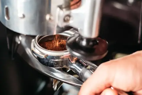 Macinatura caffè bar: polvere scura cade nel portafiltro, pronta per un espresso perfetto.