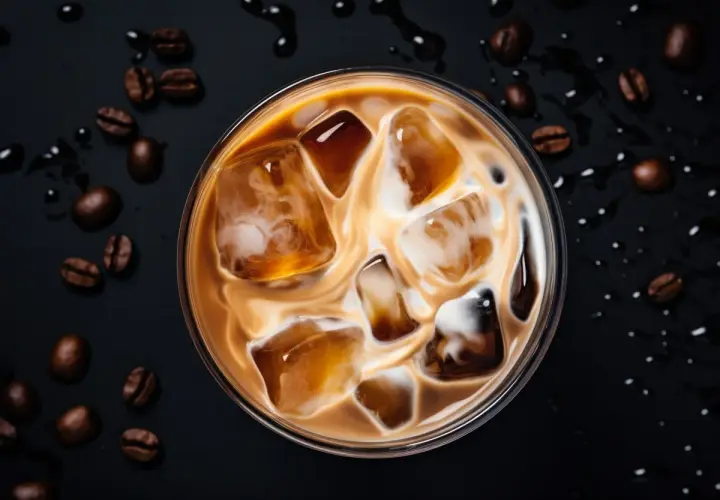 Un delizioso caffè freddo al bar, con cubetti di ghiaccio e latte che creano un vortice invitante. Chicchi di caffè tostati completano la scena.