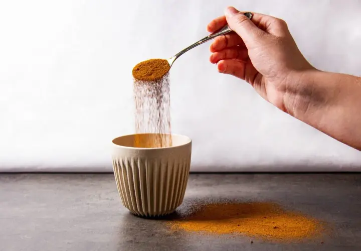 Mano versa polvere da un cucchiaio in una tazza. Forse è caffè solubile, ma fa male.