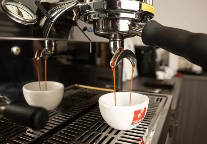 Due tazze bianche ricevono il prezioso liquido scuro, il caffè espresso, dalla macchina professionale.