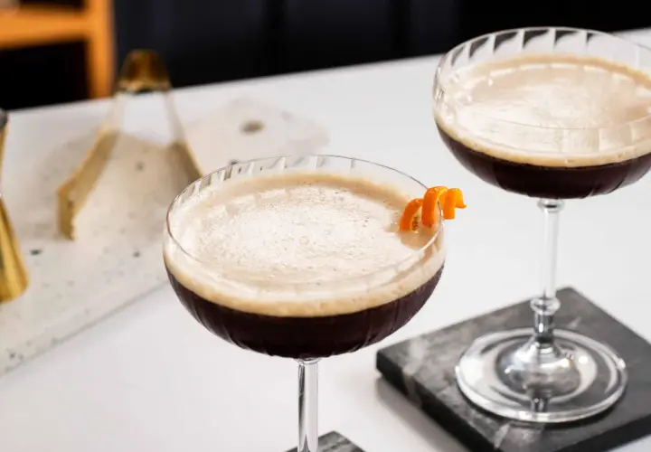 Due cocktail scuri con schiuma chiara, guarniti con scorza d'arancia. Un'idea per un caffè e succo d'arancia rivisitato.
