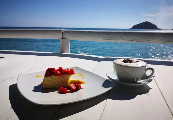 Un dolce con fragole e un caffè fumante, con il mare azzurro e un'isola all'orizzonte. Un momento di puro relax con un caffè al mare.