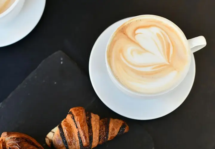 Un cappuccino con latte art a forma di cuore e croissant per una perfetta colazione al bar.