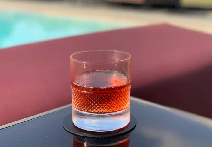 Un bicchiere di Sazerac, cocktail IBA, riposa su un tavolino vicino a una piscina.