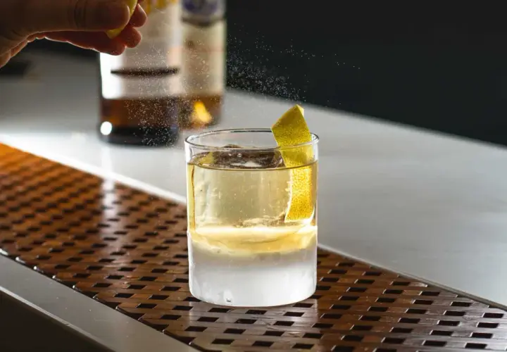 Un barista completa la negroni ricetta bar con una scorza di limone. Ghiaccio e liquore dorato in un bicchiere.