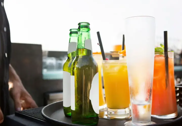 Un cameriere serve un aperitivo originale: birre fresche e cocktail colorati su un vassoio.