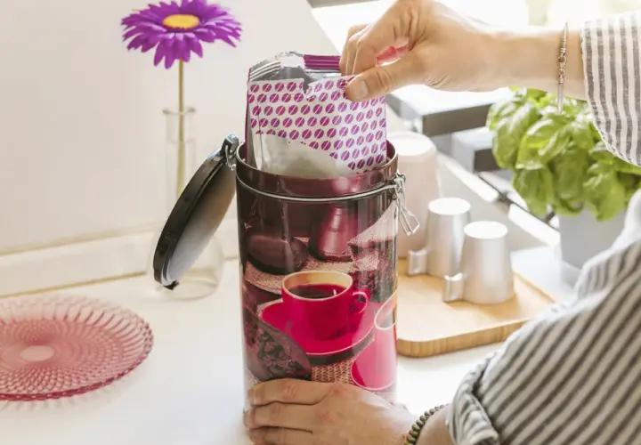 Mano inserisce pacchetto di caffè sottovuoto in un barattolo decorato. Freschezza garantita!