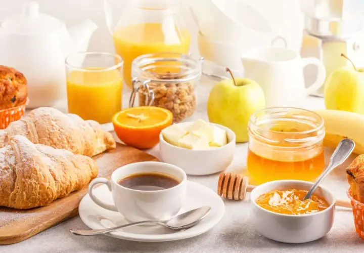 Un tavolo imbandito con croissant, caffè, succo d'arancia, frutta e marmellata, perfetto per delle bevande per colazione.
