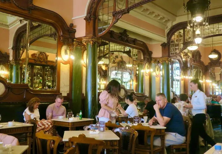 Interno di un **majestic cafe porto** con arredi d'epoca, specchi e clienti seduti ai tavoli.
