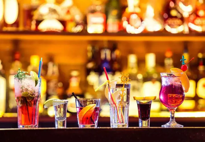 Varietà di cocktail principali colorati e rinfrescanti, guarniti con frutta e cannucce, su uno sfondo di bottiglie illuminate.
