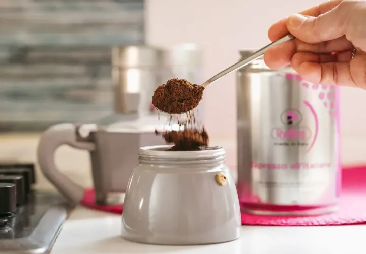 Un cucchiaino di caffè macinato cade nel bricco di una caffettiera, un ricordo di come si faceva il caffè prima della moka.