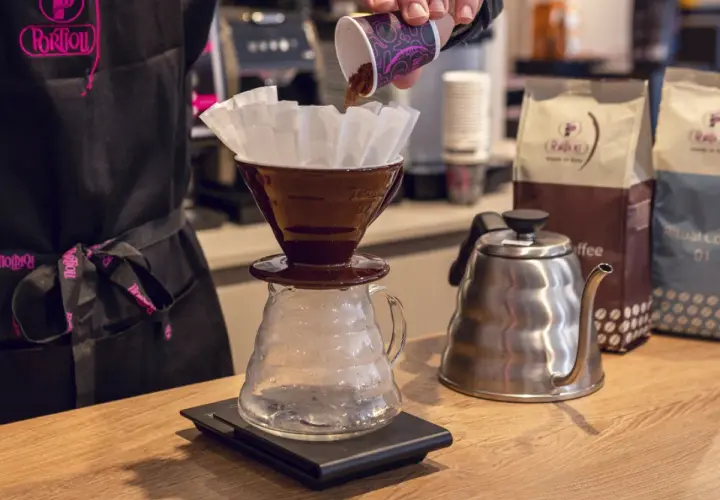 Preparazione di un caffè drip. Caffè macinato versato in un filtro, bollitore e sacchetti di caffè sullo sfondo.