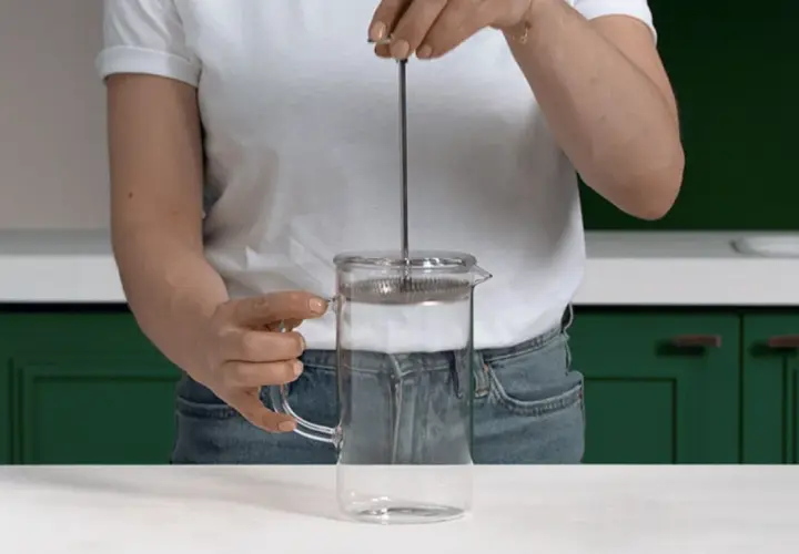 Mano che preme lo stantuffo di una french press di vetro, pronta per un caffè aromatico.