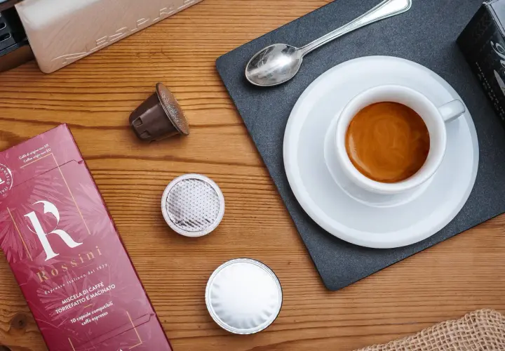 Vari tipi di caffè in capsule, una tazzina di espresso fumante e la confezione Rossini.