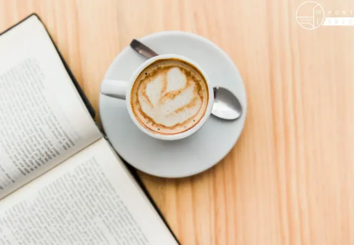 Un libro aperto e una tazza di caffè con schiuma, un invito al caffè illuminismo, su un tavolo di legno.