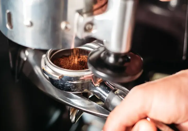 Macinatura caffè bar: polvere scura cade nel portafiltro, pronta per un espresso perfetto.