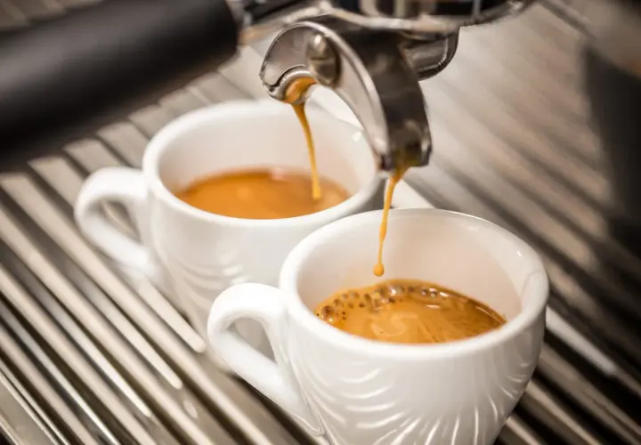 Due tazzine di caffè espresso vengono riempite da una macchina, ma il sapore bruciato del caffè rovina l'esperienza.