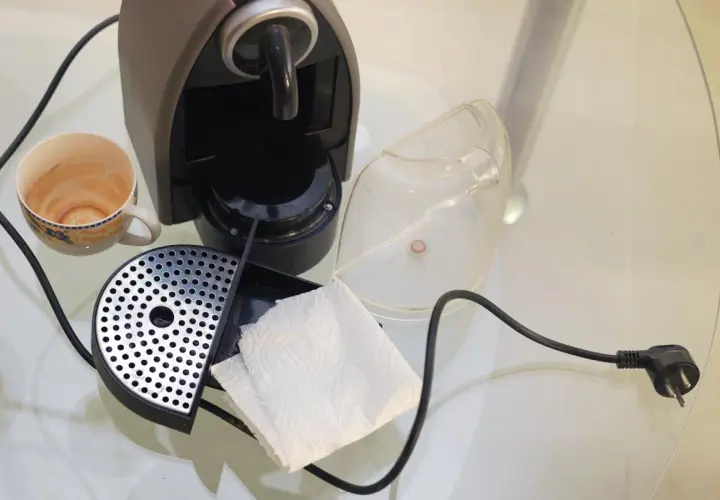 Macchina caffè bar smontata per pulizia: tazzina sporca, vaschetta raccogligocce, serbatoio trasparente e fazzoletti di carta.