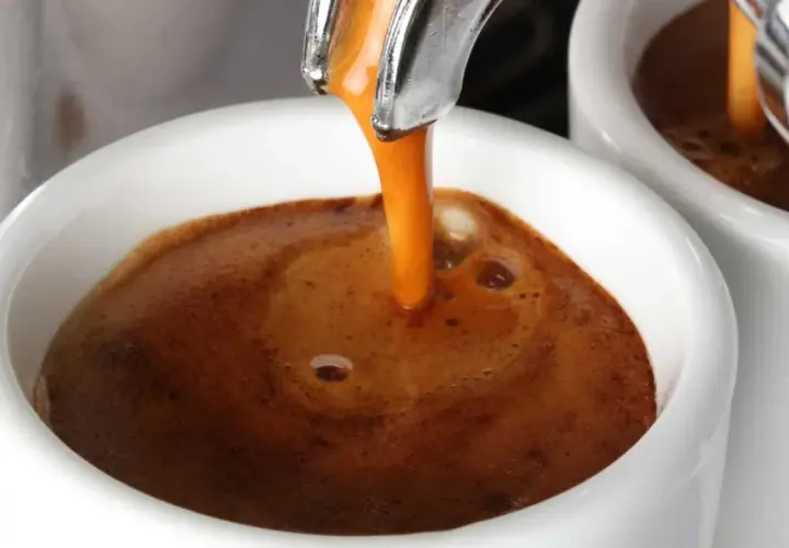 Un filo dorato di caffè caldo si riversa in una tazzina bianca, creando una crema invitante. Un buon caffè per iniziare la giornata.