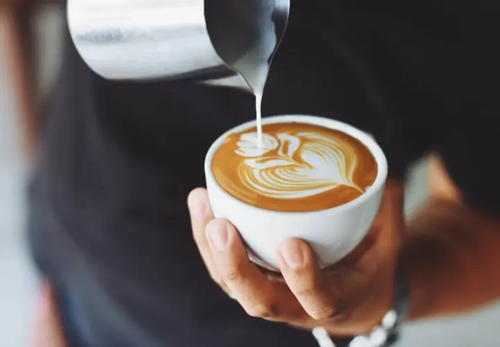 Un barista versa latte montato su un espresso, creando un disegno di latte art. Ecco come si fa il cappuccino perfetto.