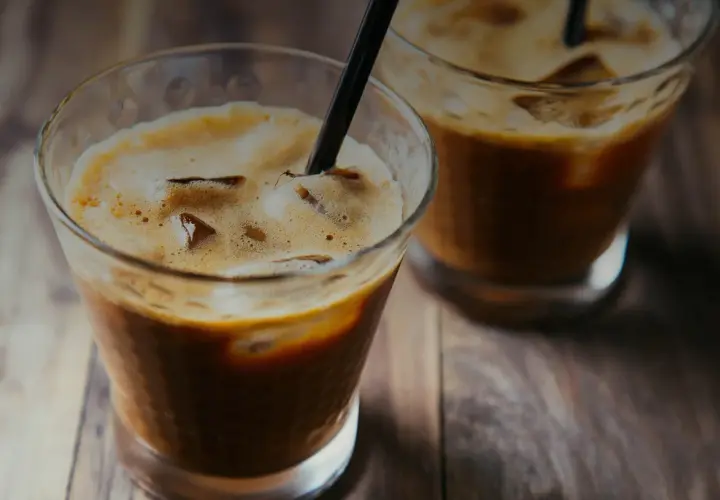 Due bicchieri di **cold brew** con ghiaccio e cannucce nere su un tavolo di legno.