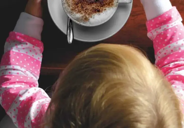 Bambini che gustano un caffè decaffeinato, con una tazza di cappuccino spolverato di cacao.