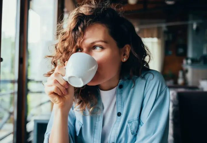Donna con capelli ricci beve una tazza di caffè, un momento di relax con potassio naturale.
