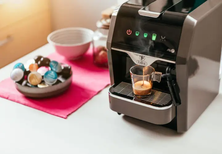 Macchina da caffè prepara un espresso. Accanto, una ciotola piena di capsule colorate, per scegliere se è meglio cialde o capsule.