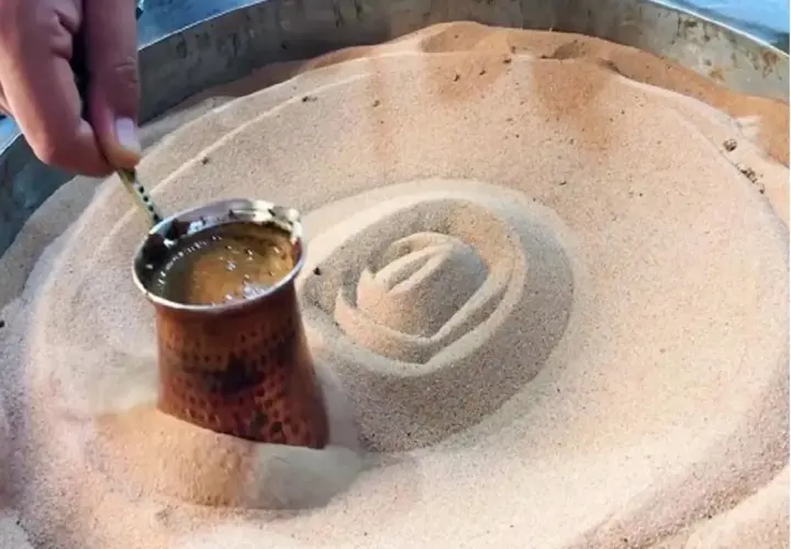 Un cezve di caffè turco viene preparato nella sabbia calda, creando un vortice invitante.
