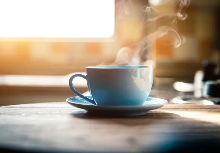 Tazza azzurra fumante su un tavolo di legno. Nonostante il suo aspetto invitante, il caffè è cancerogeno.