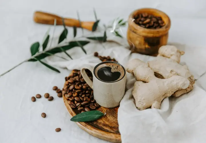 Tazza di caffè messicano fumante, chicchi tostati, zenzero fresco e un rametto d'ulivo su un panno di lino.