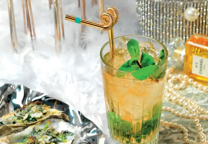 Un rinfrescante cocktail Italia, con menta e ghiaccio, accanto a ostriche gratinate e un flacone di profumo Chanel.