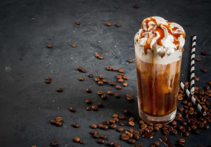 Un delizioso frappe al caffè con panna montata e sciroppo al caramello, circondato da chicchi di caffè tostati su sfondo scuro.