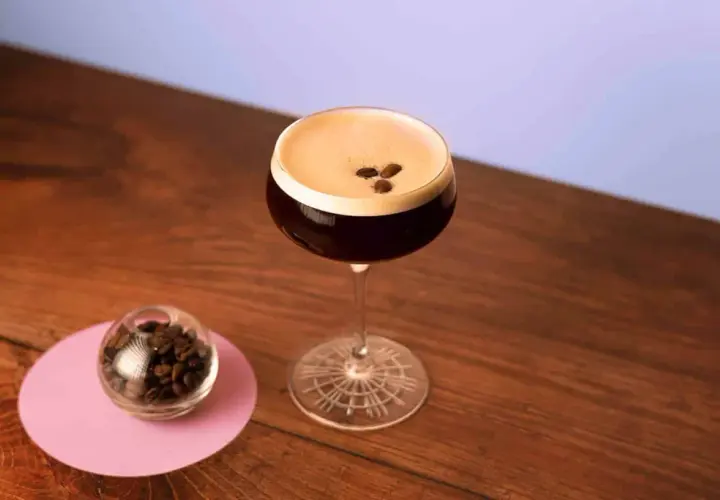 Un elegante cocktail espresso martini, con chicchi di caffè a guarnire, accanto a una piccola sfera di vetro piena di chicchi.