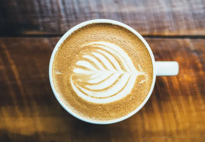 Un cappuccino con latte art su un tavolo di legno. Chissà chi ha inventato il cappuccino, ma questa tazza è perfetta.