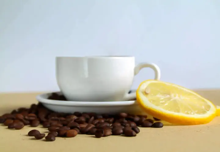 Tazzina di caffè con chicchi sparsi e una fetta di limone, un contrasto di sapori per iniziare la giornata.