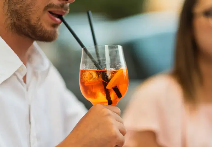 Un uomo sorseggia un Aperol Spritz, perfetto per la sua aperitivo ricetta. Ghiaccio e arancia completano il drink.