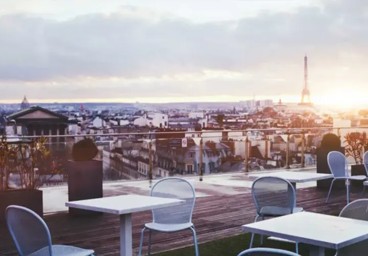 Terrazza con vista su Parigi al tramonto, tavoli e sedie vuoti, la Torre Eiffel sullo sfondo. Un luogo perfetto per godersi i locali storici di Parigi.
