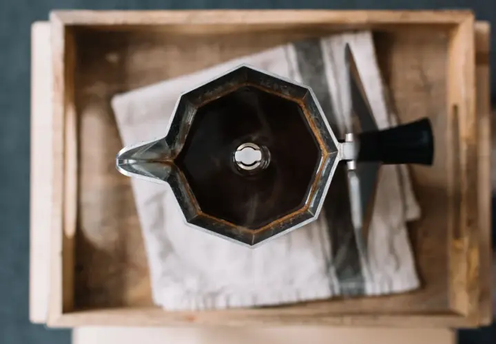 Moka nuova, appena usata, con caffè fumante, appoggiata su un panno a righe in una cassetta di legno.